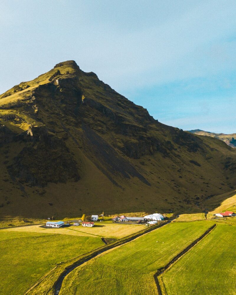 green grass field near mountain under blue sky